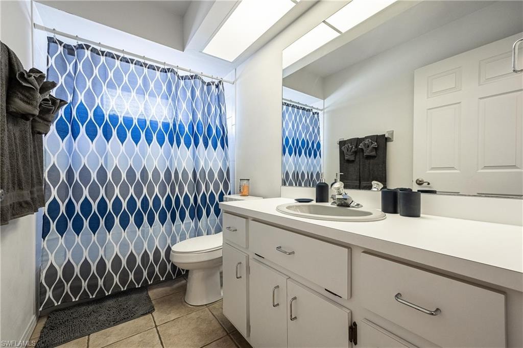Full bath with a shower with curtain, vanity, tile patterned flooring, and toilet