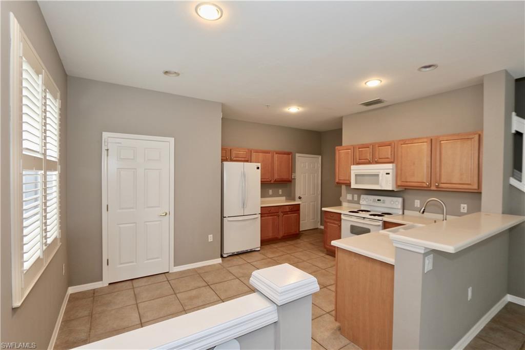 Kitchen featuring wood cabinetry, white appliances, light-toned countertops, and tile flooring