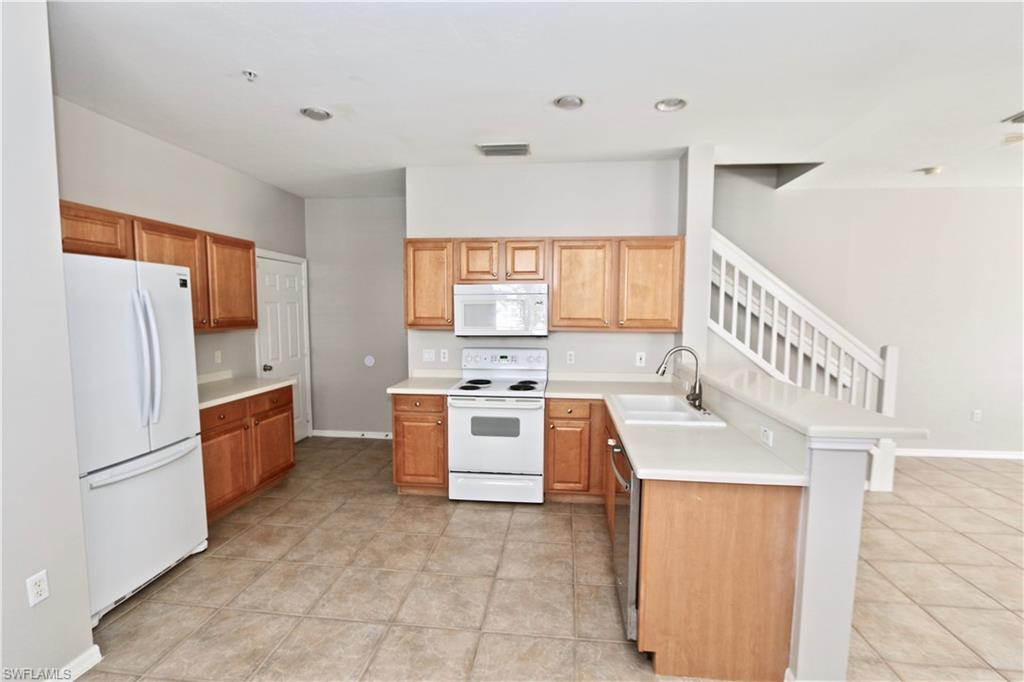Kitchen featuring wood cabinetry, white appliances, light-toned countertops, a dual basin sink, and ceramic tile flooring