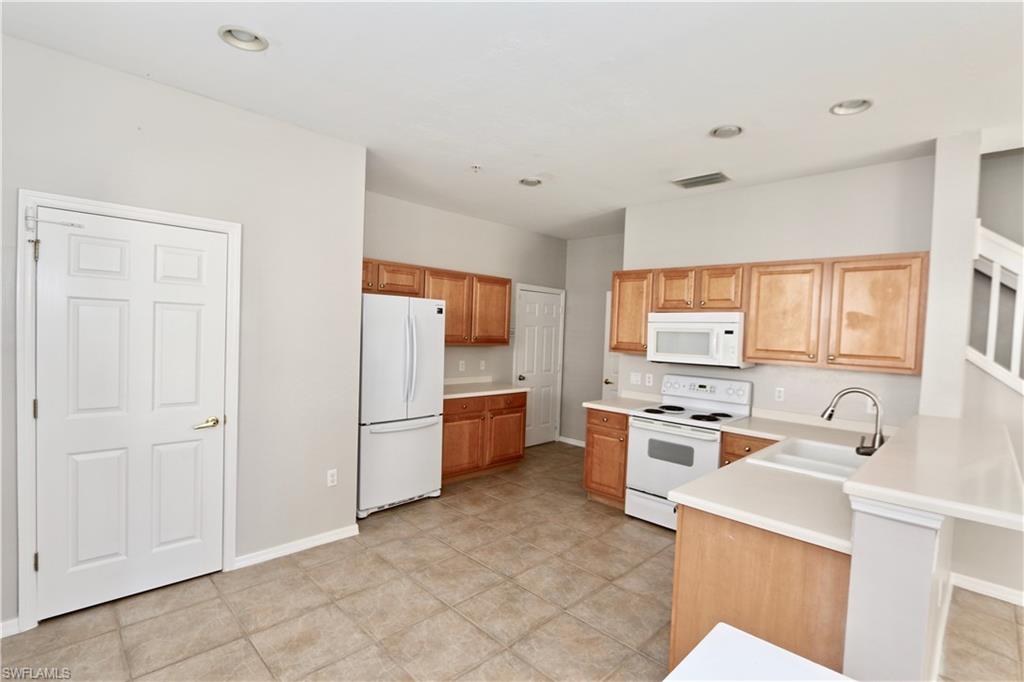 Kitchen featuring wood-finish cabinetry, tile flooring, white appliances, and a double basin sink