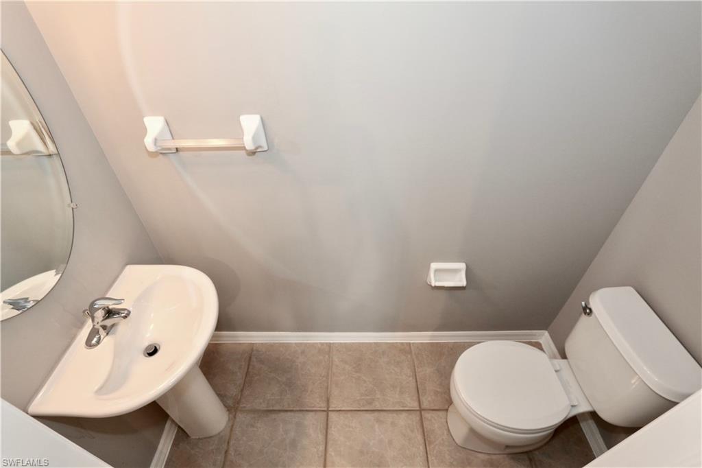 Pedestal sink with chrome faucet, circular wall mirror, and neutral tile flooring