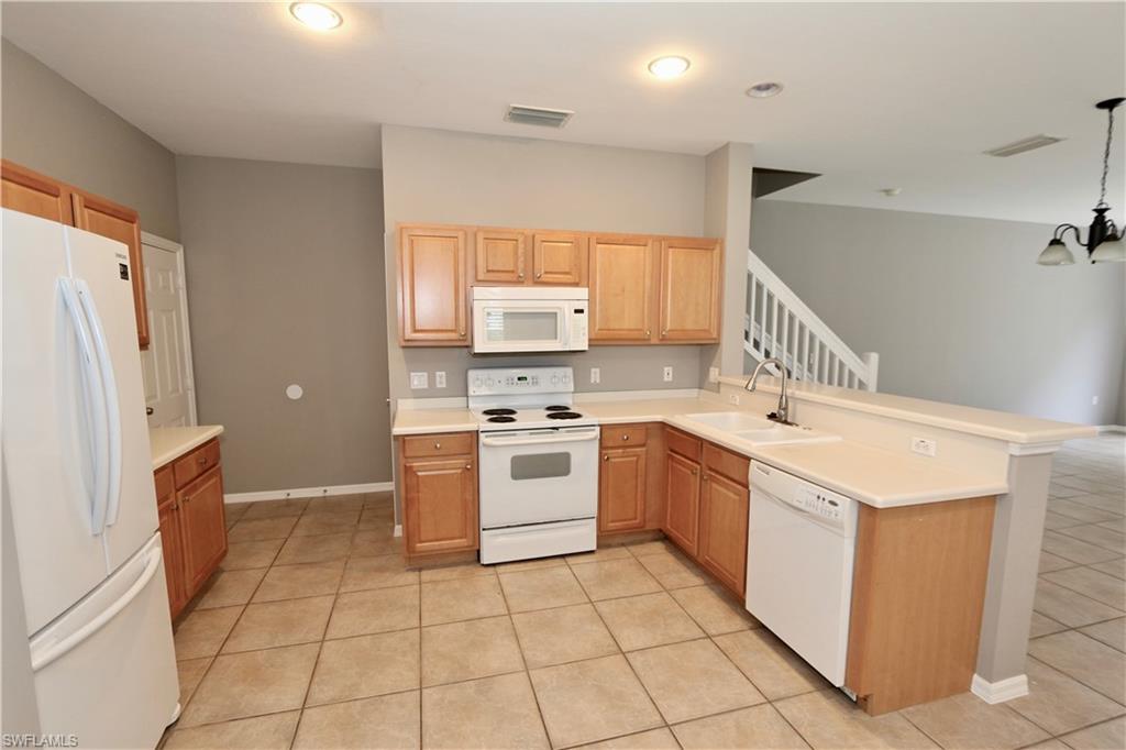 Kitchen with wood-finish cabinetry, white appliances, and a double basin sink