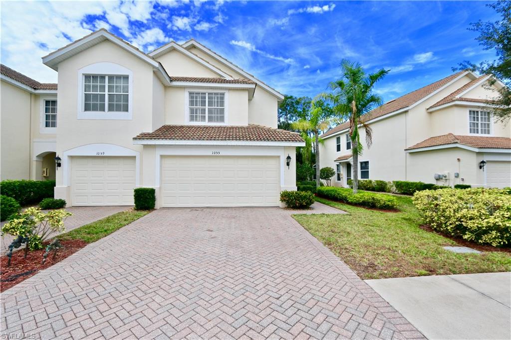 Stucco exterior featuring dual garages, a tile roof, and a paver driveway