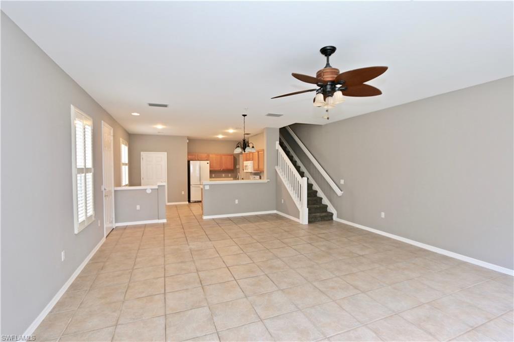 Expansive tile flooring, integrated ceiling fan with lighting, multiple windows with plantation shutters, staircase with white railing, and recessed lighting