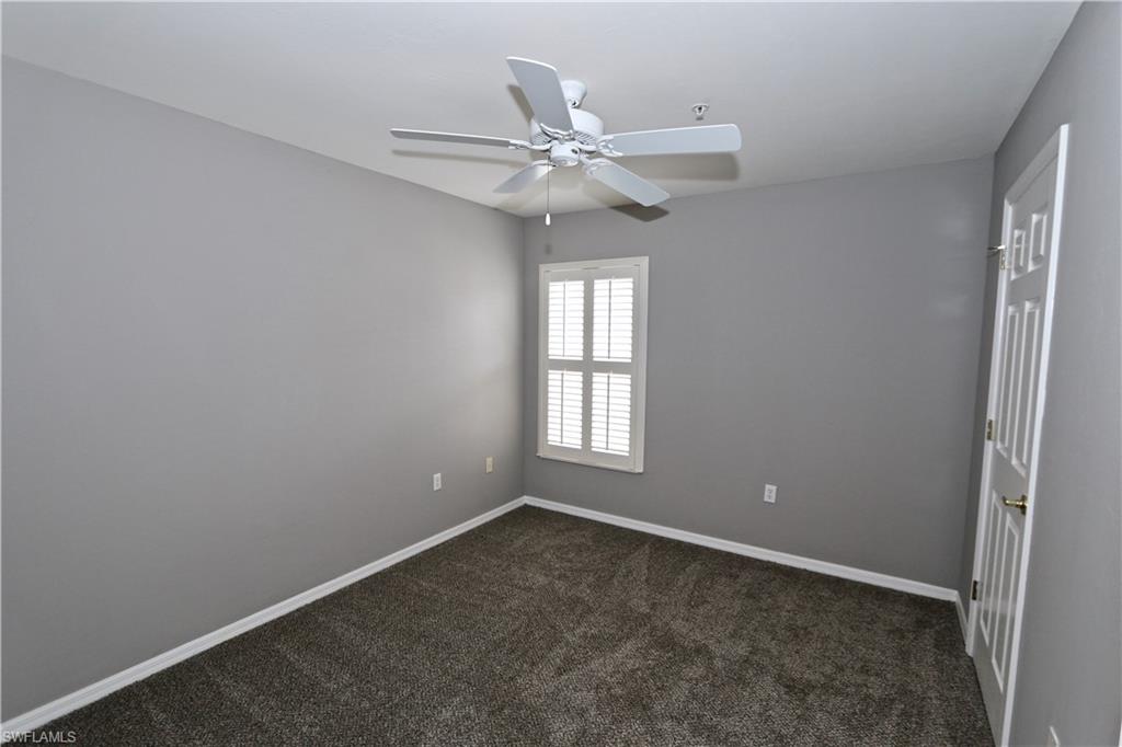 Neutral gray wall finish, textured carpeting, white plantation shutters, ceiling fan, and paneled door