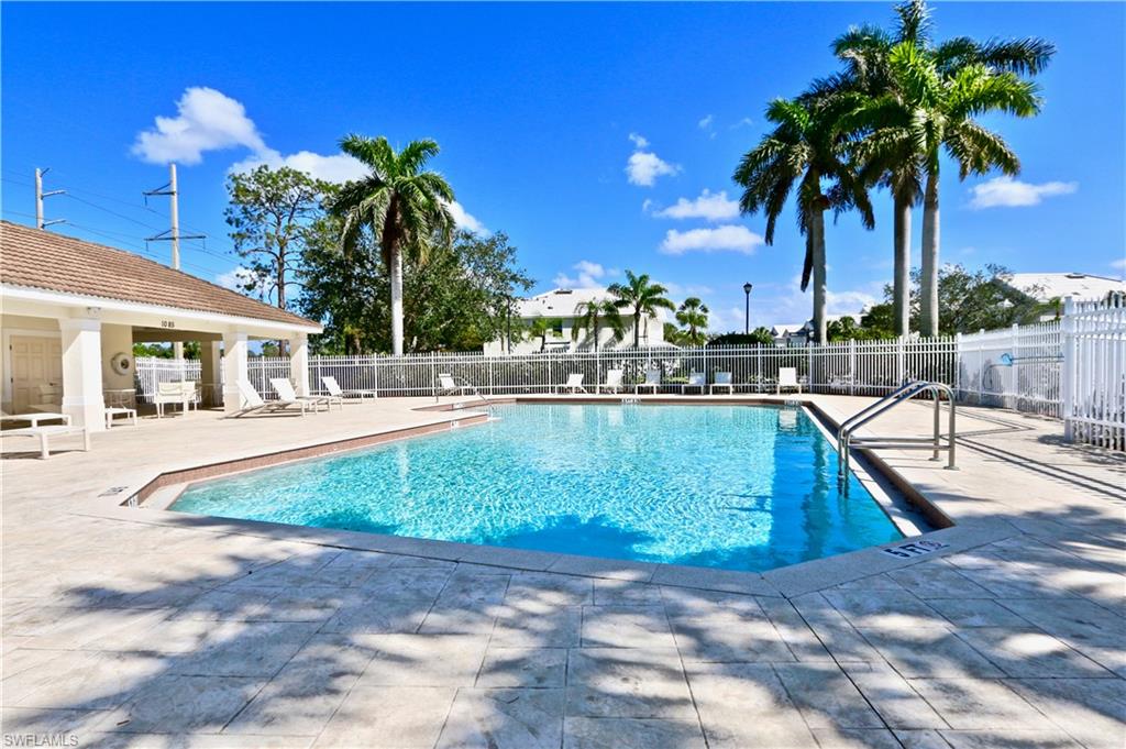 Community swimming pool with a tiled perimeter, integrated steps, and a white perimeter fence