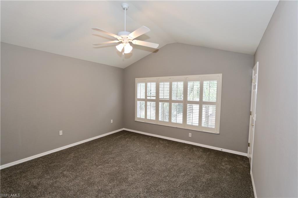 Vaulted ceiling, white ceiling fan with light fixture, plantation shutters, wall-to-wall carpeting, and neutral wall tones