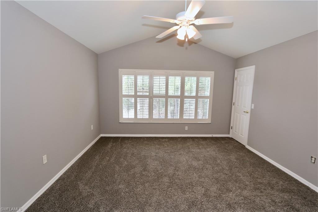 Vaulted ceiling, ceiling fan, neutral wall paint, white plantation shutters, and carpeted flooring
