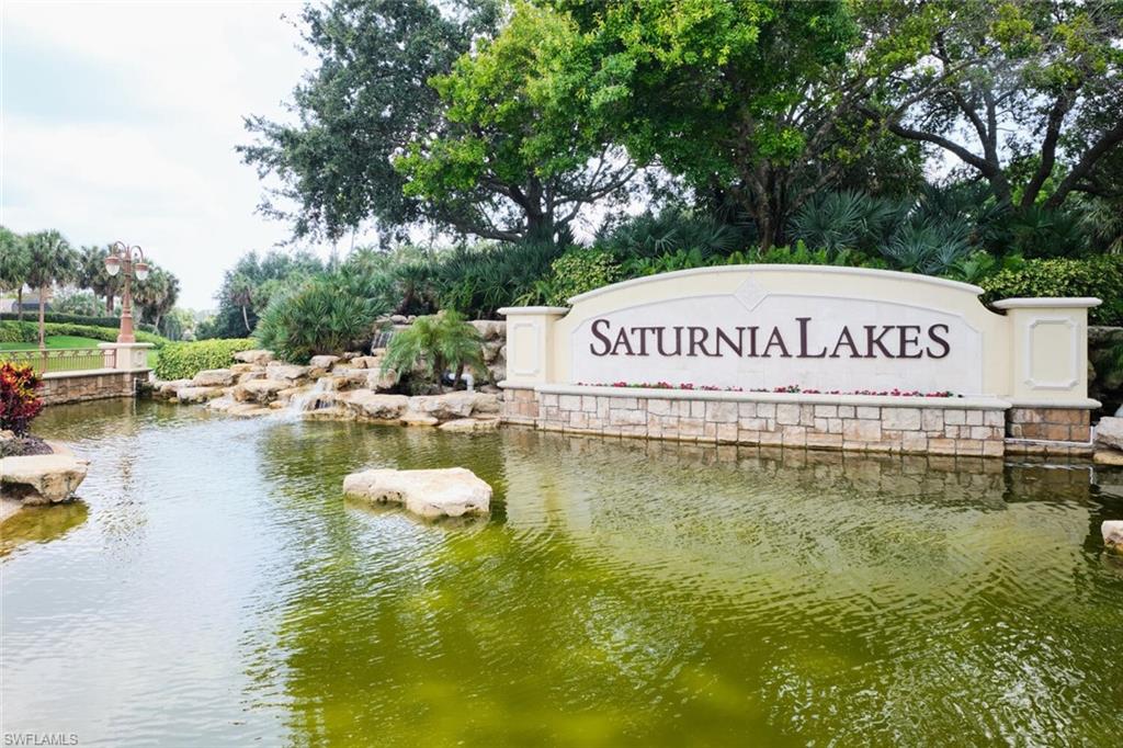 Community entrance signage with stone detailing, a water feature, and mature landscaping