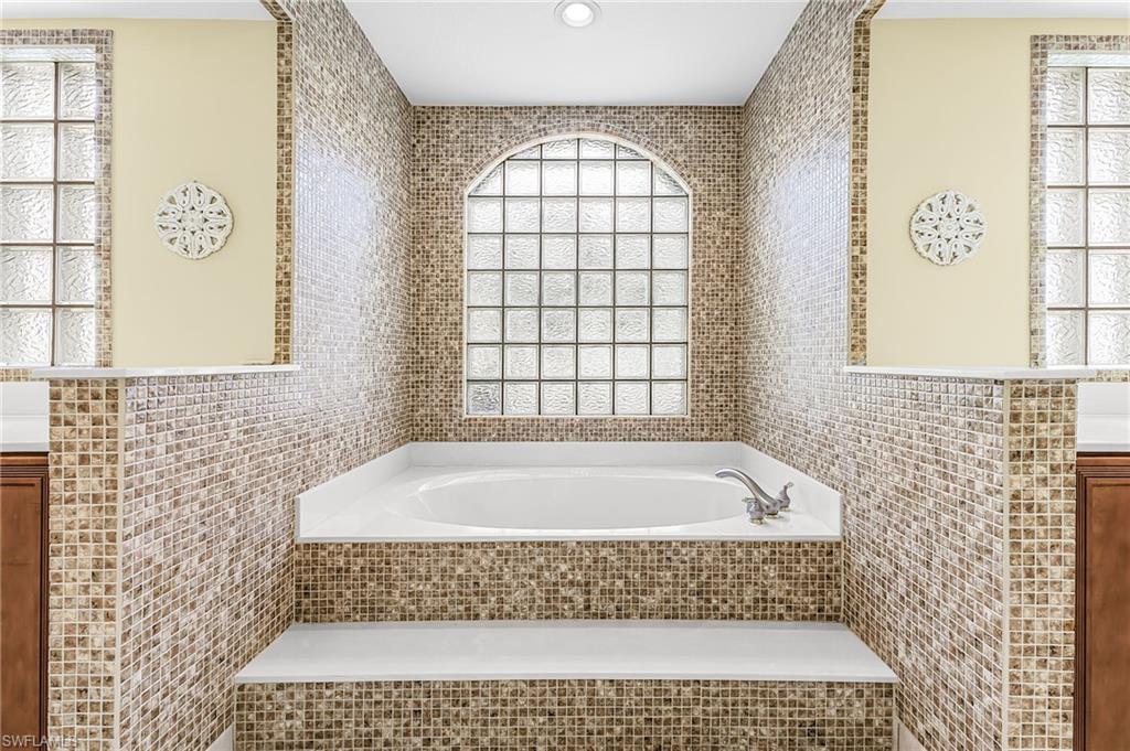 Built-in tub with mosaic tile surround, arched glass block window, and dual privacy windows