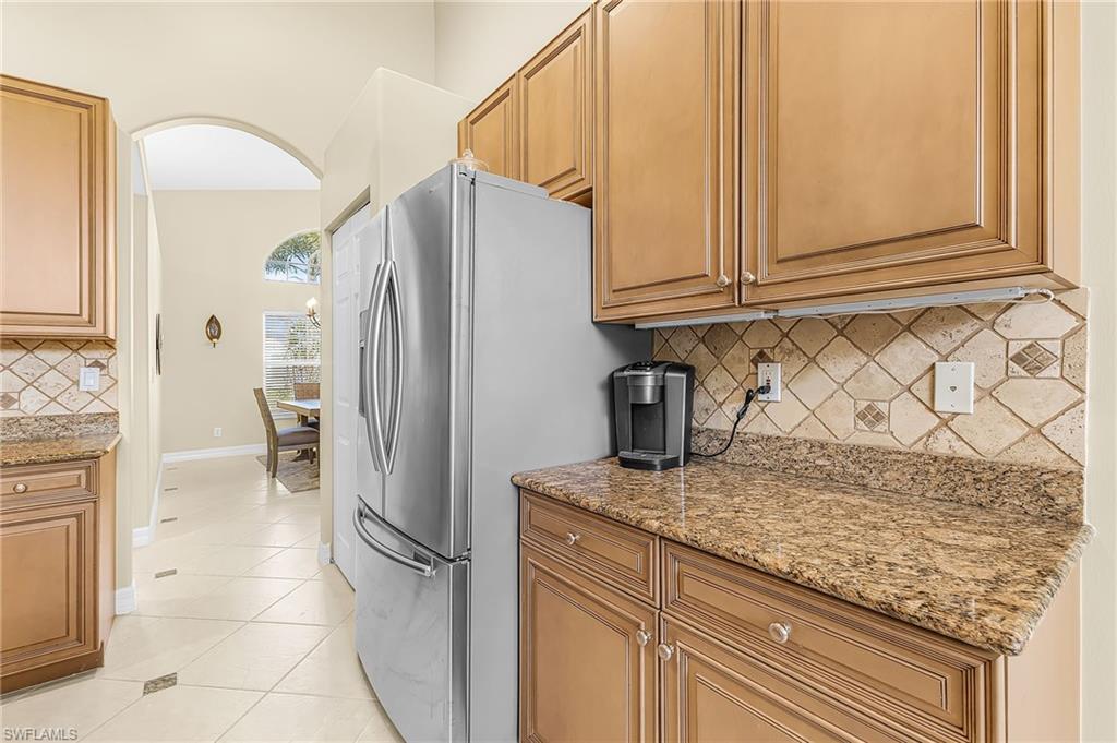 Kitchen with wood cabinetry, stainless steel refrigerator, granite countertops, and tiled backsplash