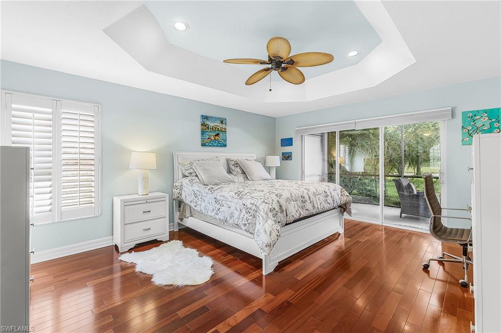 Tray ceiling with recessed lighting and a ceiling fan, wood-finish flooring, sliding glass doors to a screened patio, and window with plantation shutters