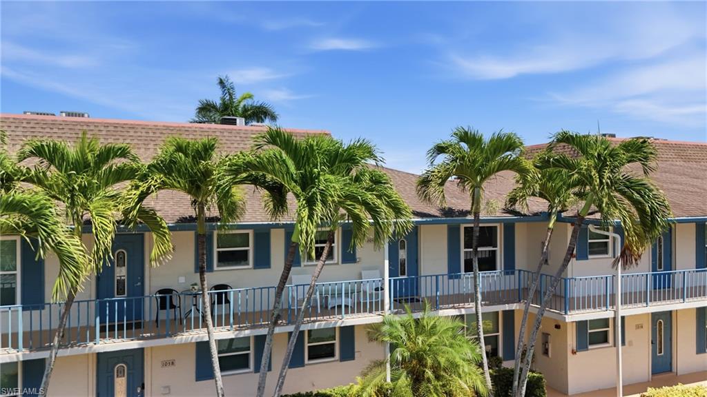 Multi-level building with individual entrances, balconies with blue railings, and abundant palm trees
