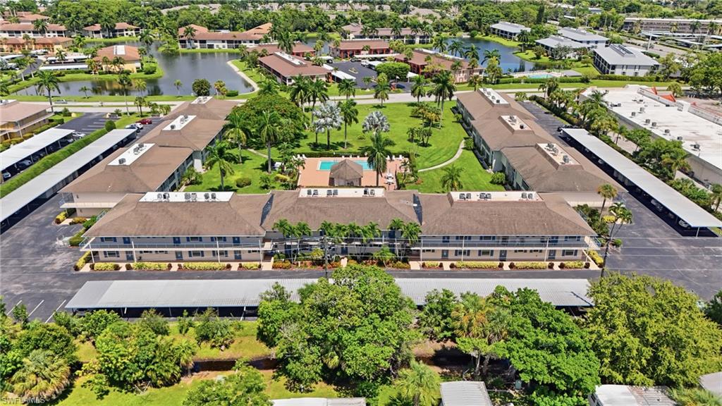 Community featuring multiple residential buildings, covered parking structures, a central courtyard with a swimming pool, and surrounding green spaces with mature trees