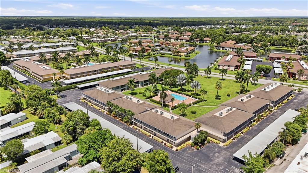Community setting featuring multiple residential buildings, paved parking areas, a swimming pool, and landscaping with mature trees