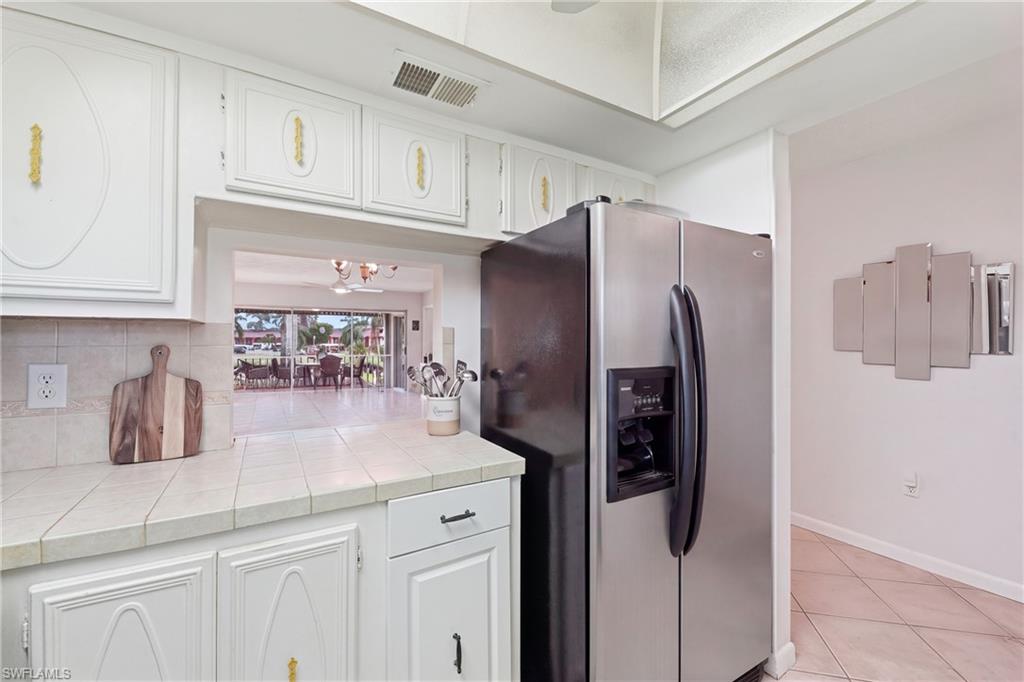 White paneled cabinetry, tiled countertops, stainless steel side-by-side refrigerator, tiled backsplash, and an interior pass-through window