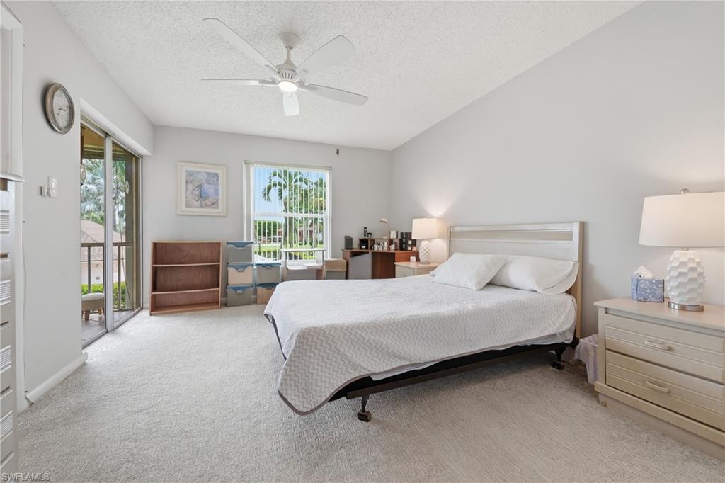 Vaulted ceiling with a ceiling fan, light-toned carpeting, ample natural light from multiple windows, and a sliding glass door leading to an outdoor area