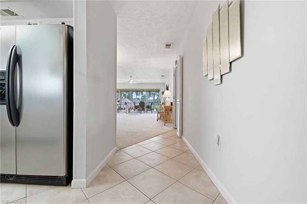 Stainless steel refrigerator, diagonal tile flooring, textured ceiling, and carpeted area