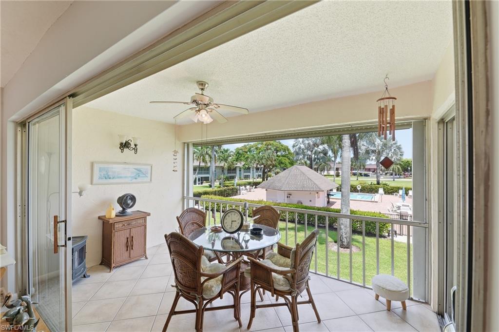 Tiled balcony featuring a ceiling fan, sliding glass doors, and a metal railing overlooking a landscaped area with a pool