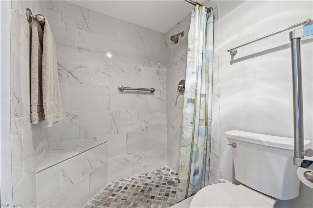 Shower with white marble-look tile, built-in corner bench, and mosaic tile flooring