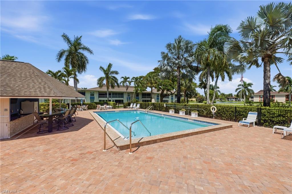 In-ground swimming pool with brick paver surround, a covered outdoor bar area, and lush tropical landscaping
