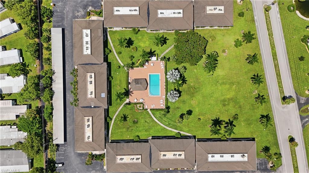 Community featuring multiple residential buildings, a central swimming pool with surrounding deck, extensive manicured lawn areas, mature palm trees, and paved parking facilities