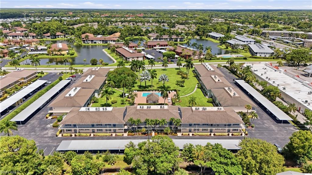Aerial perspective featuring a multi-building complex, central courtyard with a swimming pool, covered parking structures, and surrounding waterways