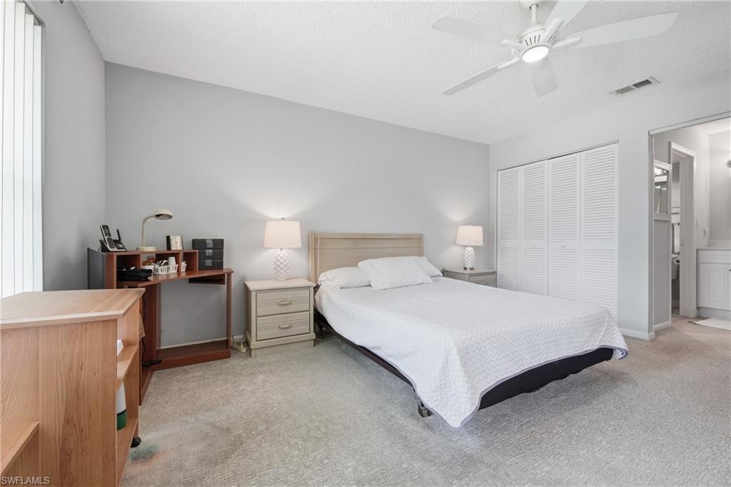 Light gray wall paint, textured ceiling, ceiling fan with integrated lighting, bi-fold louvered closet doors, and light gray carpeting