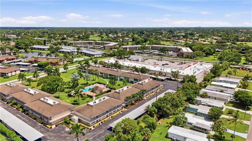 Aerial perspective of a community featuring multiple buildings with brown shingle roofs, a central swimming pool, and a pond