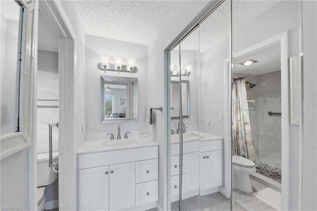 Dual vanities with white cabinetry, mirrored closet doors, and separate shower and commode areas