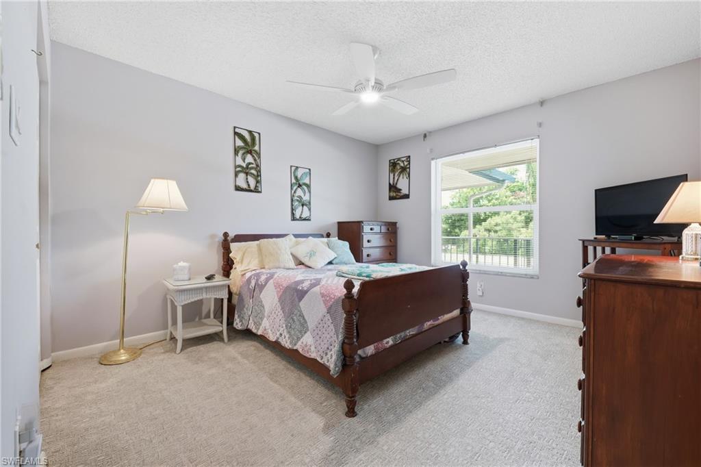 Spacious primary bedroom showcasing hardwood flooring, a wood-frame bed with decorative bedding, dual nightstands with integrated lighting, carpeted flooring in select areas, and abundant natural light from a large window with direct outdoor access