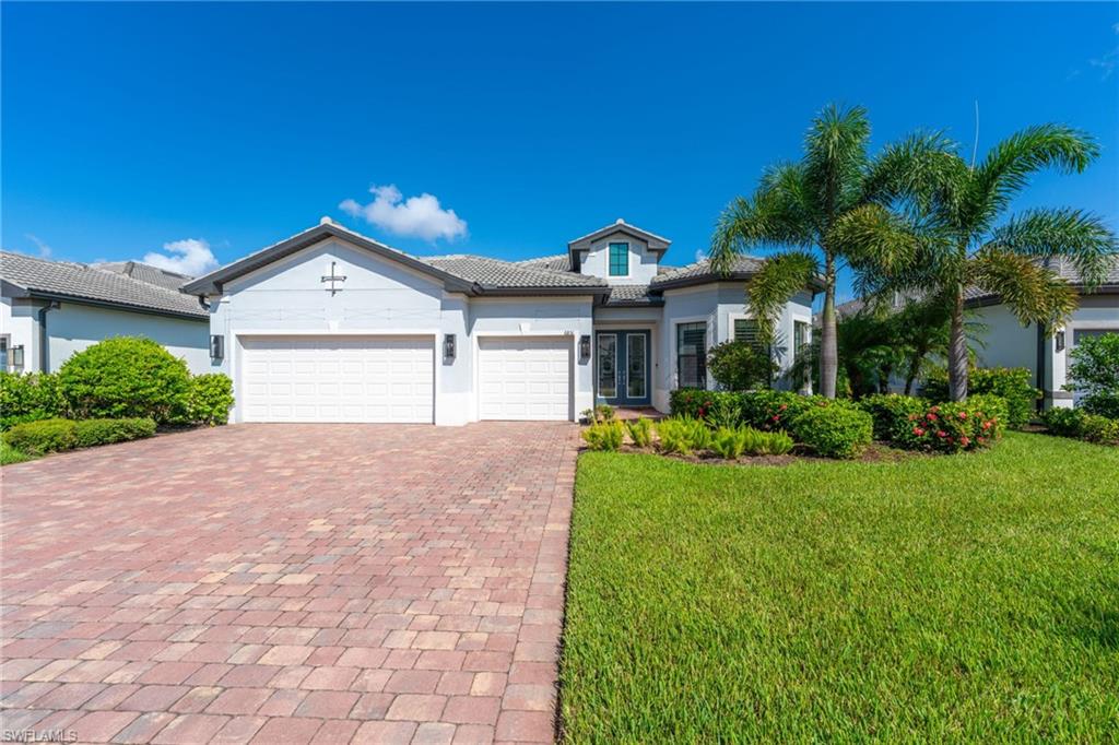 Exterior featuring a paver driveway, three-car garage, manicured lawn, and mature palm trees