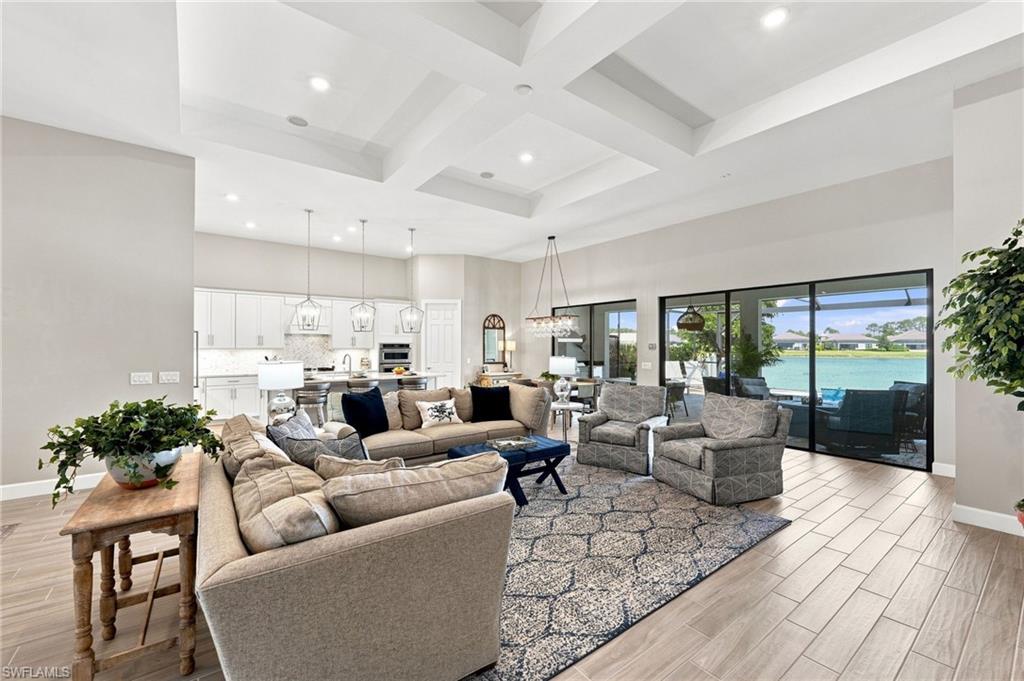Coffered ceiling with recessed lighting, wood-look tile  flooring, sliding glass doors to outdoor covered lanai, white kitchen cabinetry, and modern pendant lighting