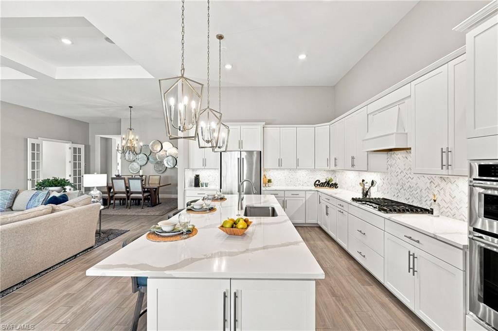 Spacious kitchen featuring an expansive island with sink, a herringbone tile backsplash, and modern lighting