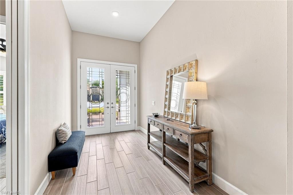 Double entry doors with decorative glass panels, recessed ceiling lighting, wood-look plank tile  flooring, and neutral wall tones throughout