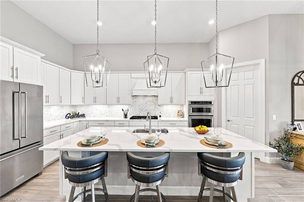 Spacious open kitchen featuring an expansive island, white cabinetry with under cabinet lighting,  modern hardware and pendant lighting