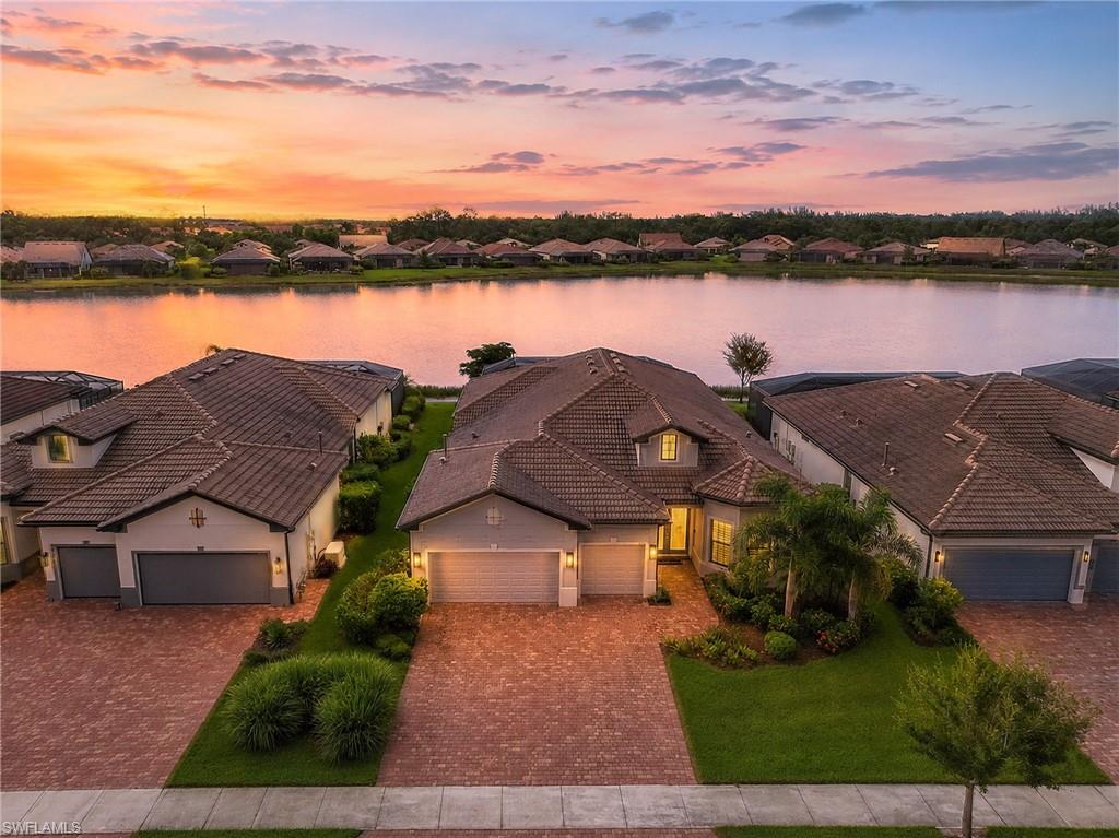 Waterfront property featuring beautiful sunset views ,tile roof, paver driveway, three-car garage, and established landscaping