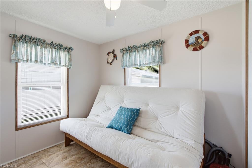 Two windows with horizontal blinds, wall paneling, tile flooring, and a ceiling fan