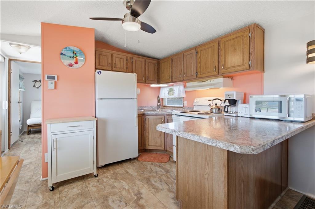 Kitchen featuring wood-finish cabinetry, a ceiling fan, and stone-look countertops