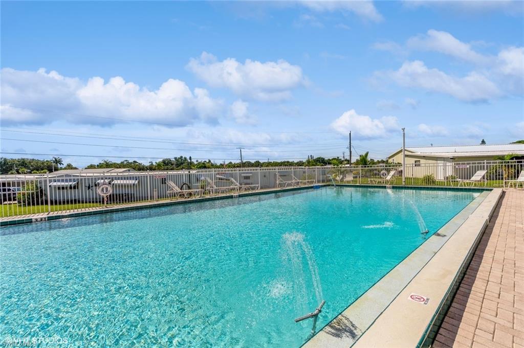 Expansive outdoor pool with a decorative fountain, surrounded by a white metal fence and paver decking