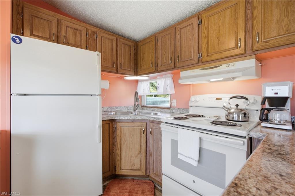 Kitchen featuring wood cabinetry, solid surface countertops, a stainless steel sink with a gooseneck faucet, and white appliances