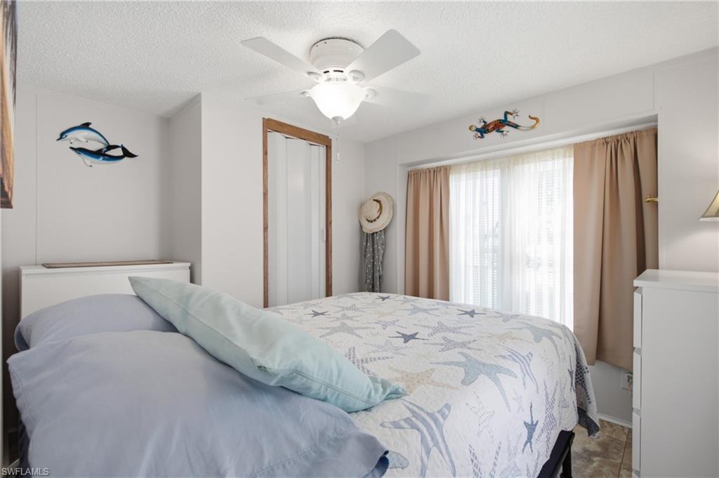 Ceiling fan with light fixture, large window with sheer and solid curtains, wood-finish flooring, and white bifold closet doors