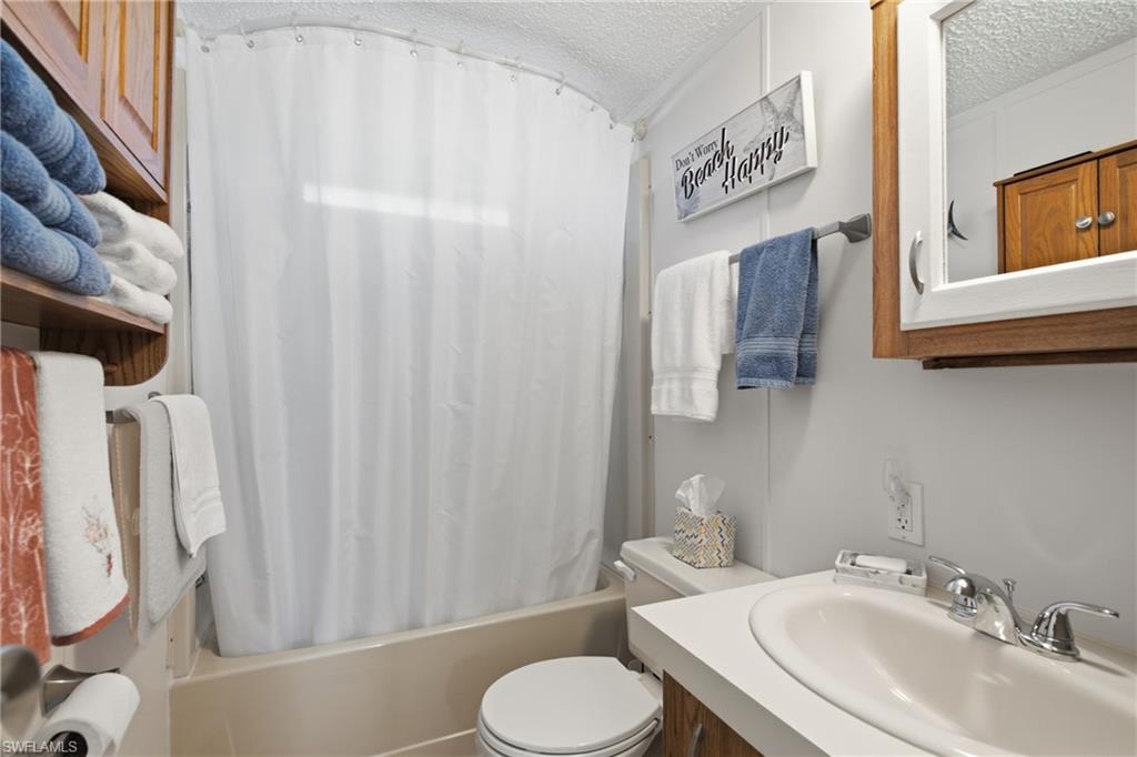 Built-in open shelving, wood-finish vanity with countertop sink, wall-mounted mirrored medicine cabinet, and tub with shower