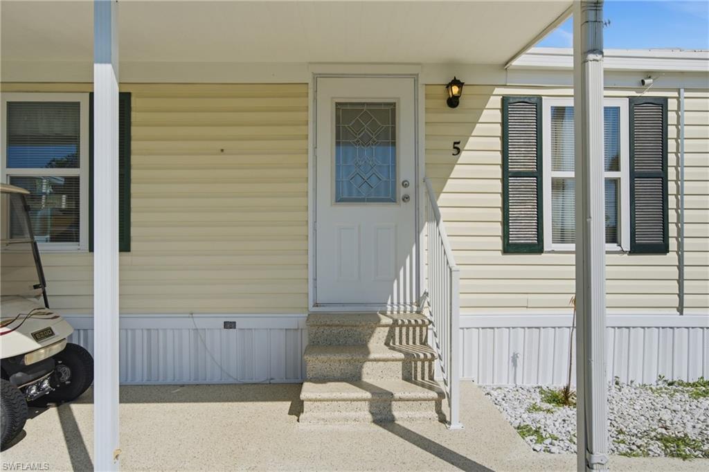 Beige vinyl siding, white entry door with decorative glass insert, textured concrete steps, dark louvered shutters, and exterior wall sconce