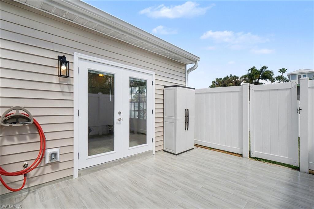Patio featuring light-toned plank-style flooring, white privacy fencing, and double glass-paneled doors