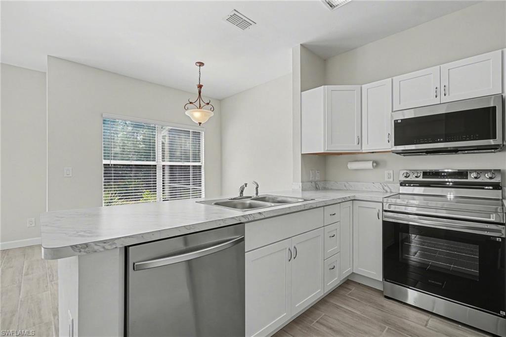 Kitchen featuring white cabinetry, stainless steel appliances, a double basin sink, light-toned countertops, and wood-finish flooring