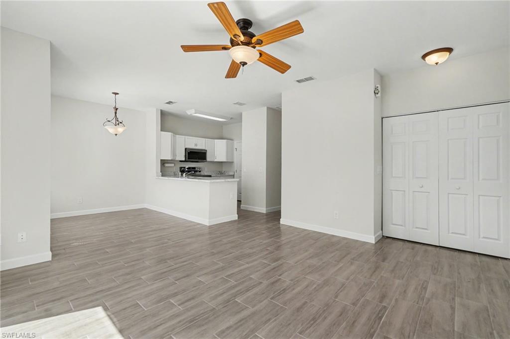 Wood-finish tile flooring throughout, featuring a ceiling fan with integrated lighting, a built-in closet with bi-fold doors, a kitchen pass-through, and white cabinetry