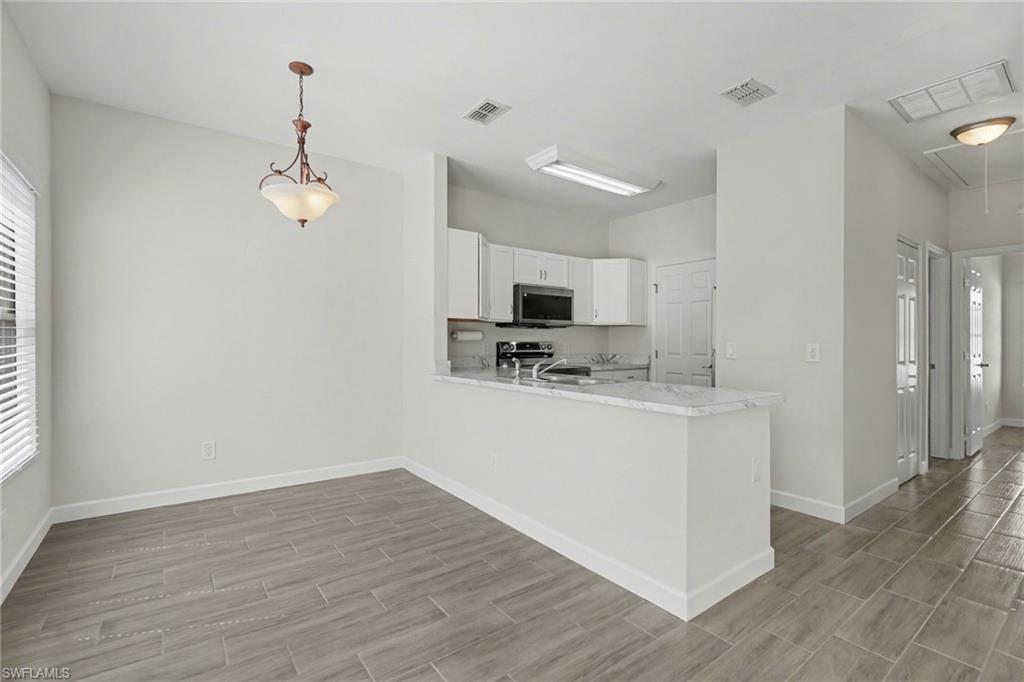 Open-concept living space featuring wood-finish flooring, white cabinetry, integrated stainless steel microwave, and a breakfast bar with a light-colored countertop