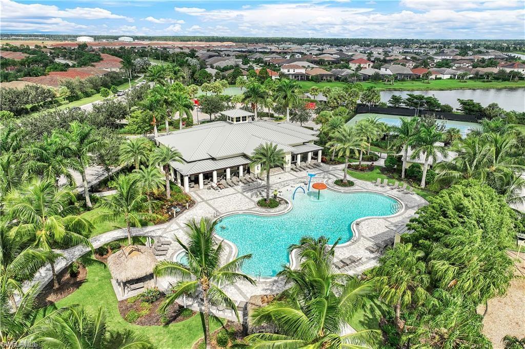 Expansive community pool with integrated splash pad, surrounding paved patio, and a central clubhouse structure