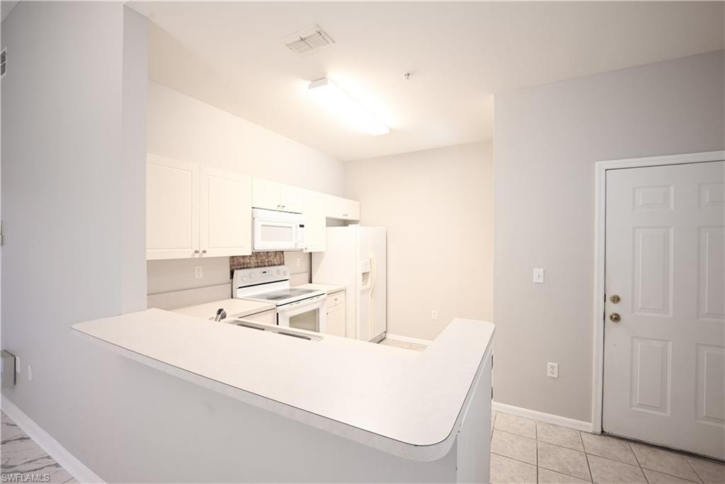 Bright kitchen featuring white cabinetry, white appliances, with breakfast bar seating, recessed ceiling lighting, and tile flooring throughout